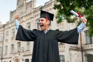 Estudante extremamente contente com sua formatura, vestindo uma beca e segurando seu diploma. Atrás, vemos um grande campus, comum às universidades