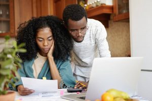 Dois estudantes universitários tentando aprender cálculo sozinhos. Eles estudam usando um computador e listas de exercícios.