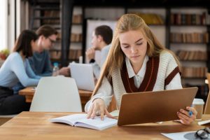 Estudante pesquisa em livros e na internet como é um trabalho na norma ABNT. Ela anota as principais normas em um caderno.