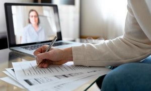 Estudante segue dicas para estudar inglês sozinho. Ele assiste a uma videoaula online enquanto faz anotações em um caderno.