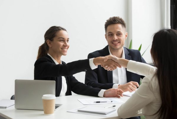 Estudante de graduação se saindo bem em uma entrevista de estágio. Os recrutadores apertam sua mão e sorriem, dando boas-vindas.