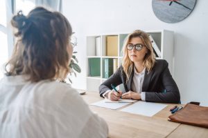 Estudante calma mostra que sabe o que falar em uma entrevista de estágio. A recrutadora anota as respostas e escuta atentamente.